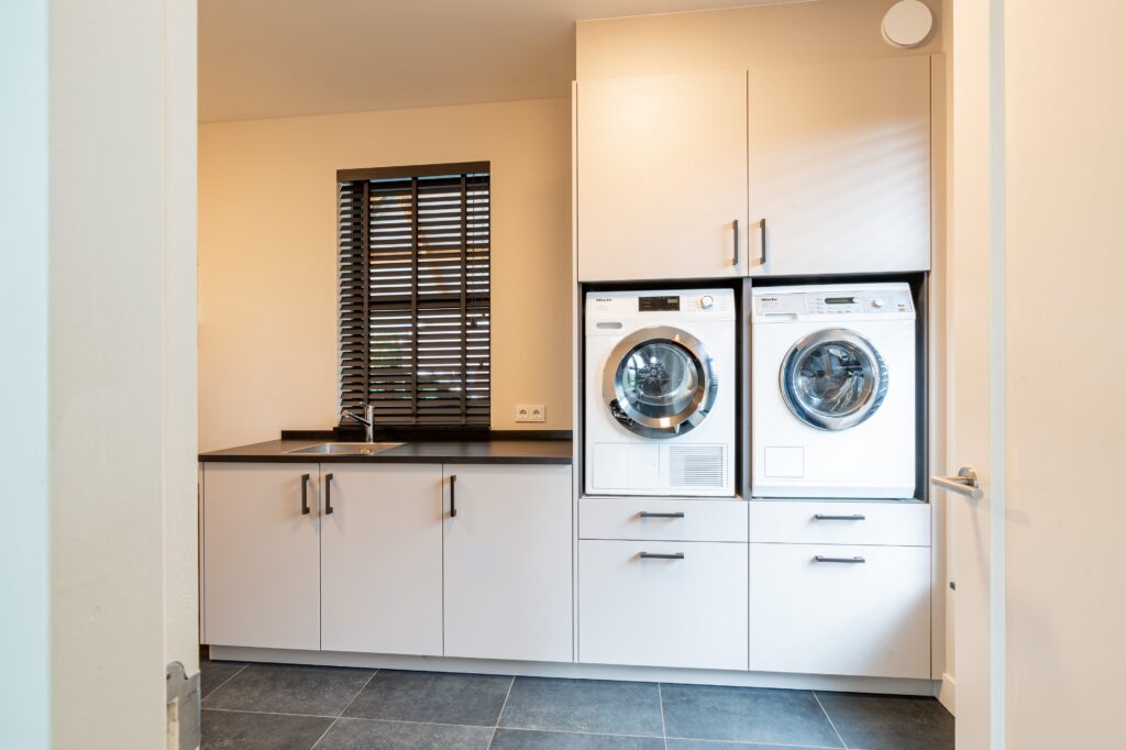 Maatwerk interieur van Mennen Keukens + Interieurs met bijkeuken voor wasmachine en droger, Mereno Monza front in kasjmier grijs kleur