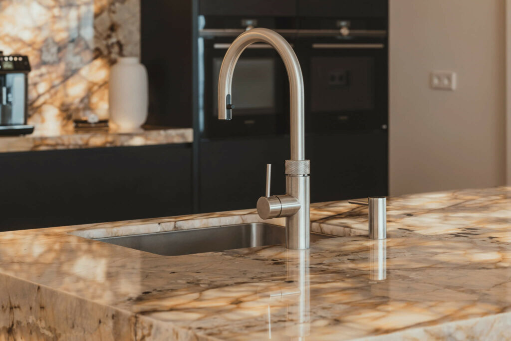 Luxe keuken van Tieleman Keukens met verlicht marmer, Mereno Monza front in matzwarte kleur detail van kraan en eiland